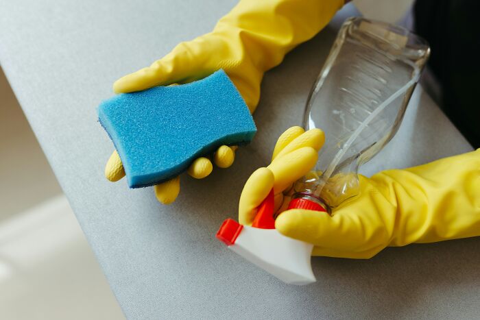 Hands in yellow gloves holding a blue sponge and a spray bottle, showcasing lesser-known cleaning hacks.