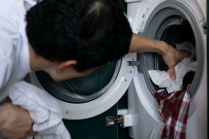 Person loading a washing machine with clothes, demonstrating a cleaning hack.