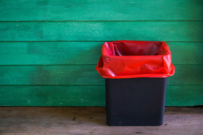 Trash can with red liner against a green wall, illustrating a cleaning hack for odor control.