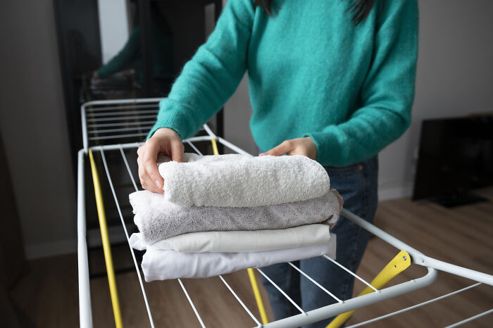 Person placing folded towels on a drying rack, showcasing a lesser-known cleaning hack for efficient space use.