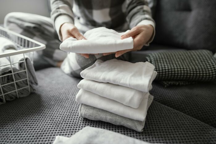 Person folding clean clothes on a bed, showcasing effective cleaning hacks.