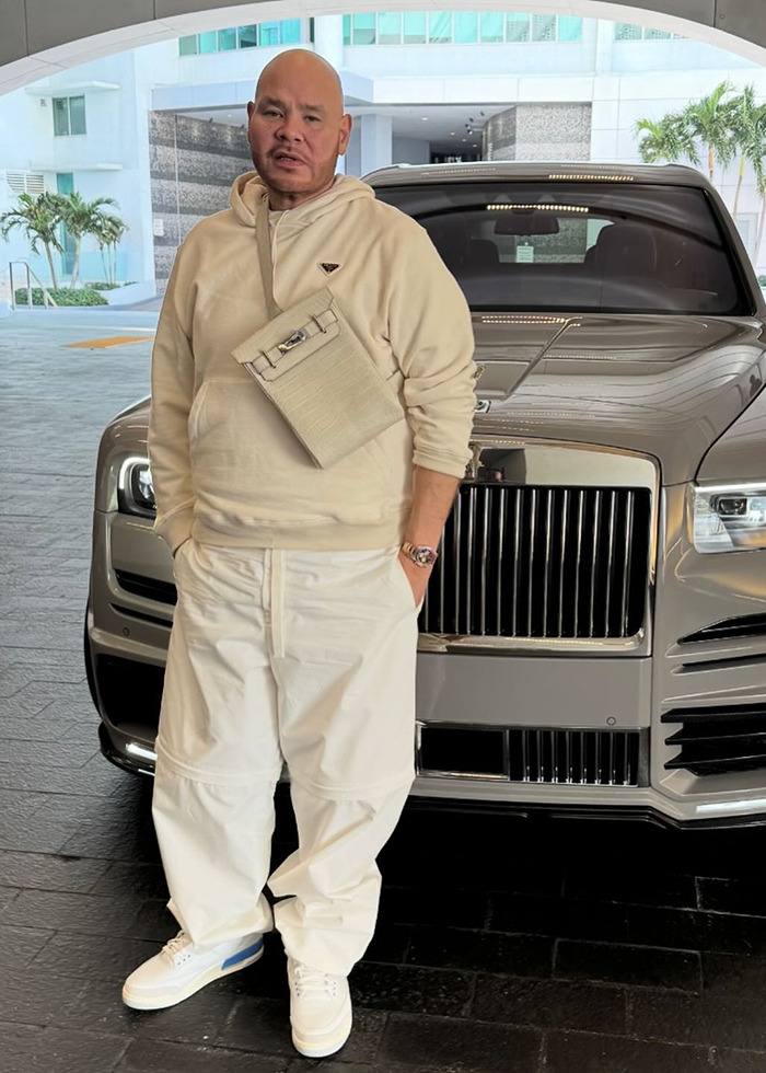 Man in cream outfit poses in front of luxury car, highlighting Hollywood beauty standards debate.