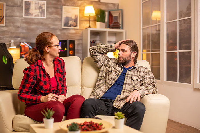 Couple having a serious discussion on the couch, expressing emotions about family planning and having children.