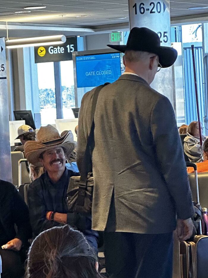 Hombre con sombrero vaquero sonriendo en una sala de espera del aeropuerto, escena divertida.