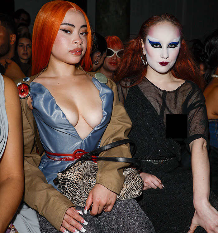 Two people sitting in fashionable outfits at Paris Fashion Week, one experiencing a wardrobe malfunction.