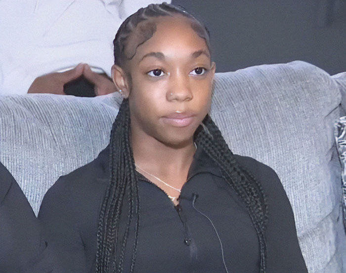 Track star in black jacket seated on a couch during an interview, addressing the incident with the baton.