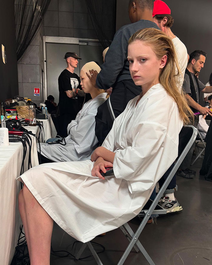 Young model in a white robe preparing backstage at Paris Fashion Week debut.