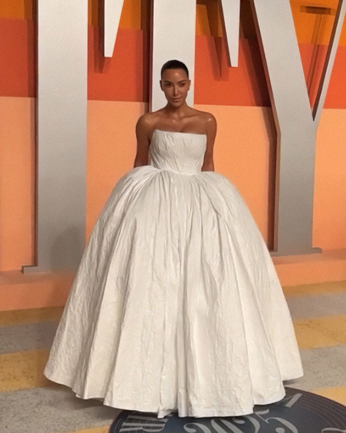 Celebrity in an elegant white gown at a formal event, posing against a colorful backdrop.