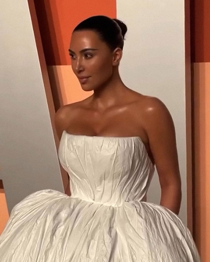 A woman in a white dress standing against an orange background.