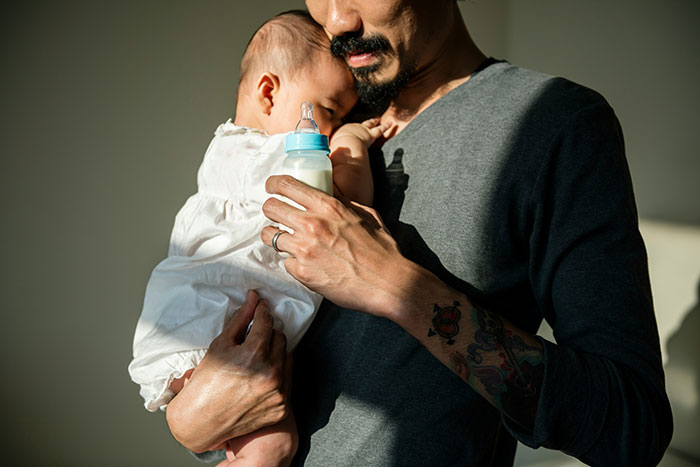 Man holding a baby with a bottle, possibly related to single motherhood dynamics.