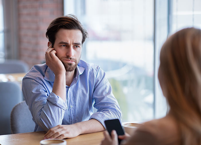 Man looks thoughtful during conversation in a cafe, holding a phone, related to dating and potential single motherhood.