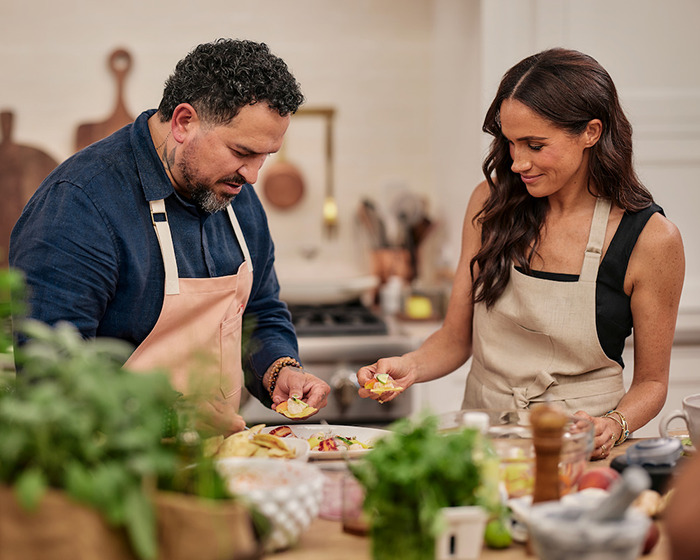 People cooking together in a kitchen, wearing aprons and surrounded by ingredients.