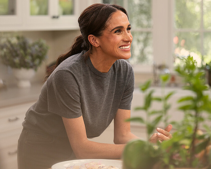 Smiling woman in a kitchen setting, surrounded by greenery and decor.