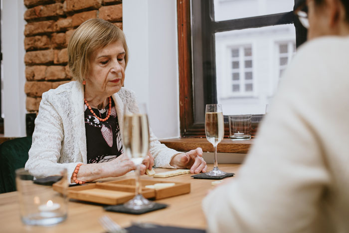 Elderly woman seated at a table with champagne, suggestive of a missing wallet scenario.