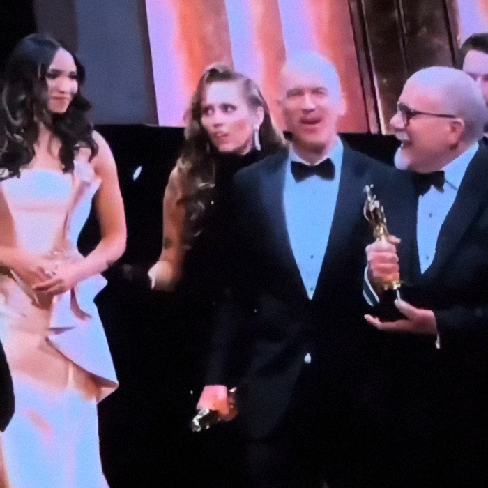 Oscars ceremony with award winners on stage, smiling and holding trophies.