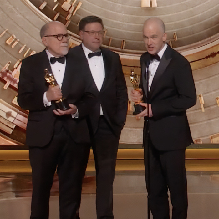 Three men in tuxedos holding Oscars on stage, related to Miley Cyrus' praised NSFW comment at the event.