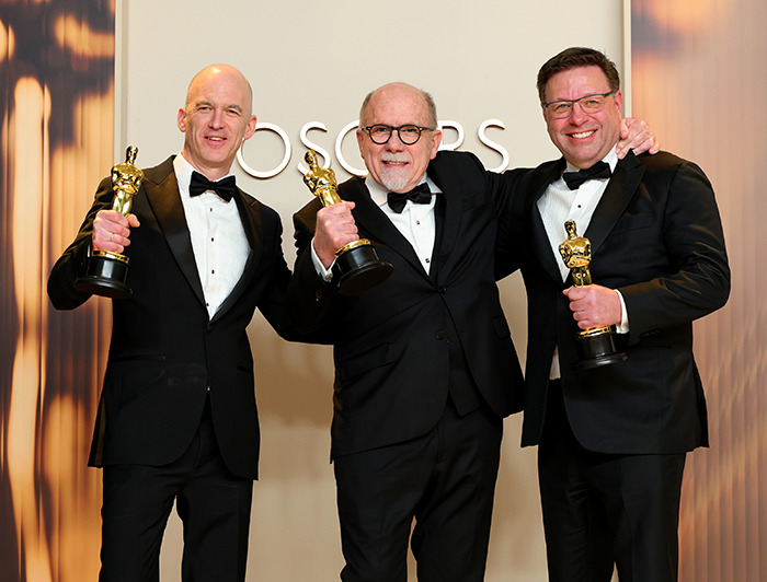 Three men in tuxedos holding Oscars trophies, celebrating a win at the Oscars.