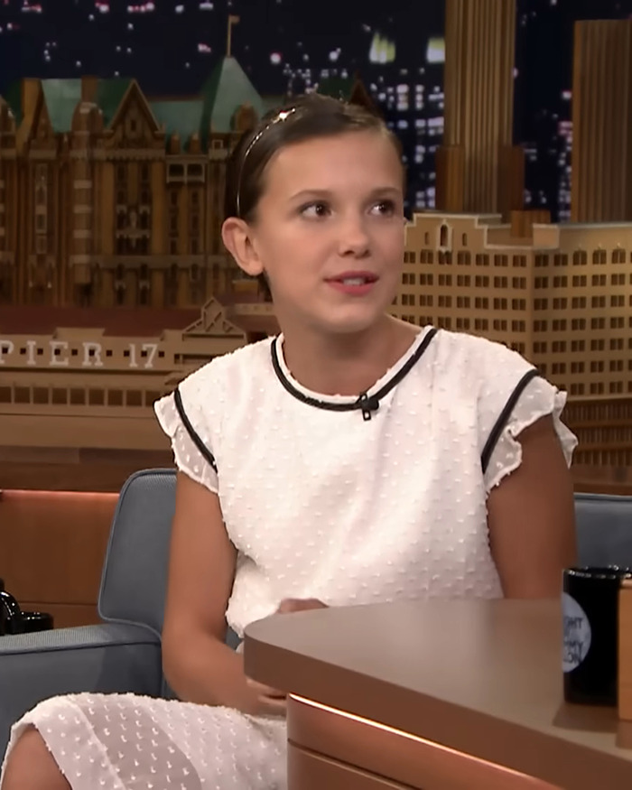 Young actress in a white dress on a talk show, discussing her experience with growing up and addressing bullying of her looks.