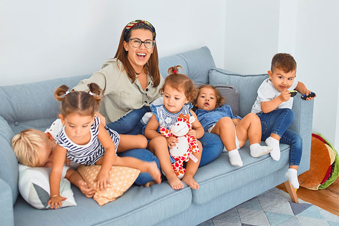 Mom with nine kids on a couch, looking overwhelmed while others are out trail running, feeling hardly stress-free.