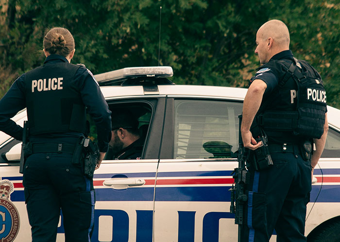 Police officers standing by a patrol car, discussing a situation related to an unhinged neighbor story.