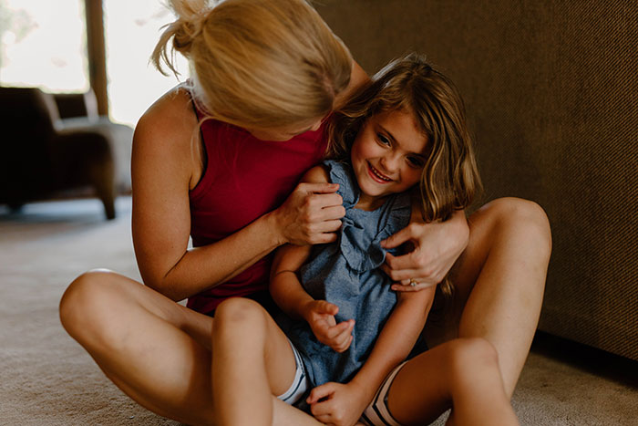 A mother playfully hugs her young daughter on the floor, highlighting the fragile nature of early childhood.