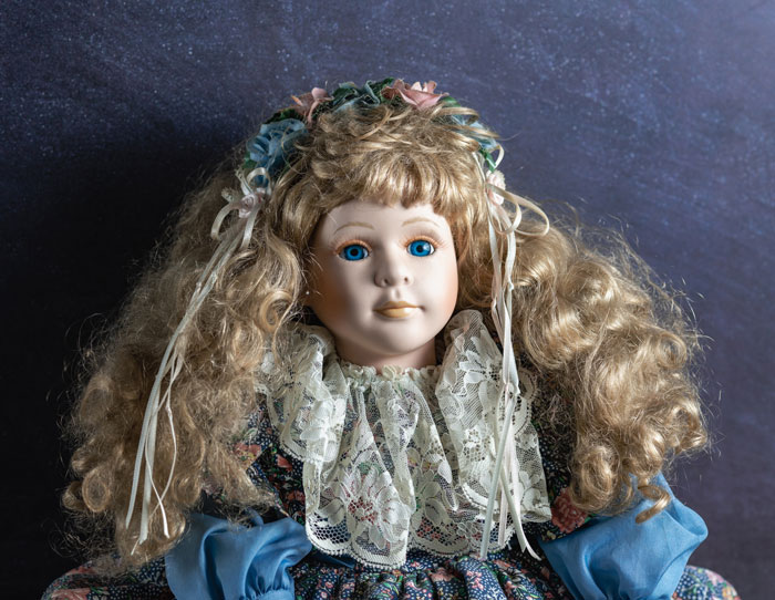 Heirloom doll with curly hair and lace dress against a dark backdrop.