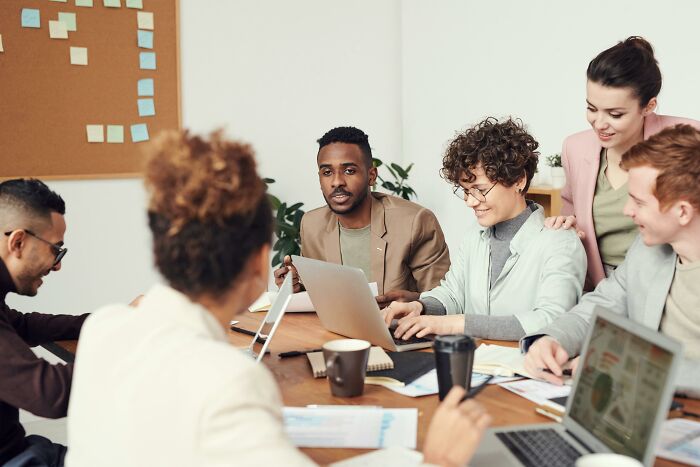 People at a work meeting around a table, displaying various expressions and gestures.