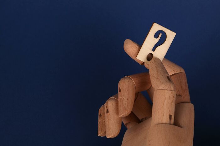 Wooden hand holding a question mark against a dark blue background, symbolizing the Mandela Effect challenge.