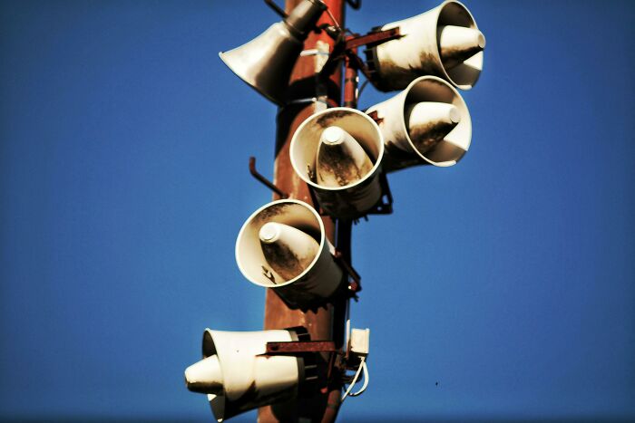 Loudspeakers clustered on a pole against a clear blue sky, related to cool Wikipedia articles.