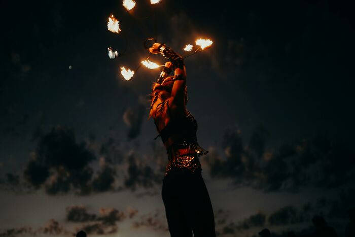 A fire performer skillfully juggles flaming torches against a dark evening sky, creating a captivating display.