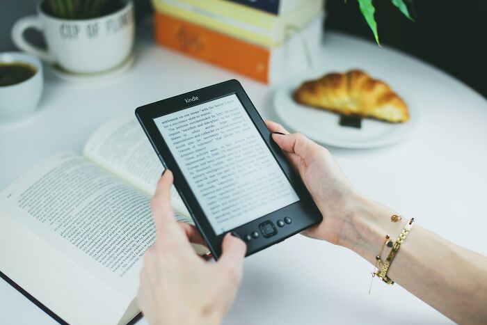 Hands holding an e-reader with an open book and croissant nearby, suggesting valuable memberships for readers.