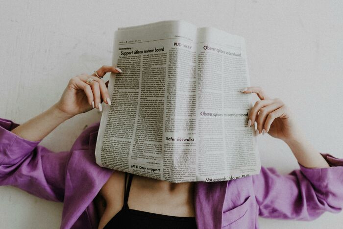 Person in purple jacket reading, with newspaper covering face, suggesting distraction similar to cool Wikipedia articles.