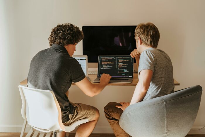 Two people collaborating at a desk with laptops, discussing cool Wikipedia articles, with code on the screens.