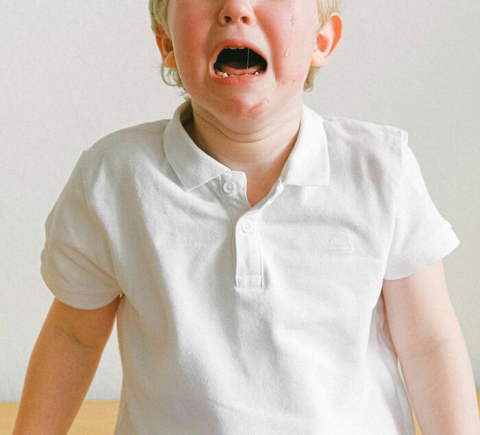 A child in a white polo shirt, crying with tears running down his face, capturing a random moment in the world.