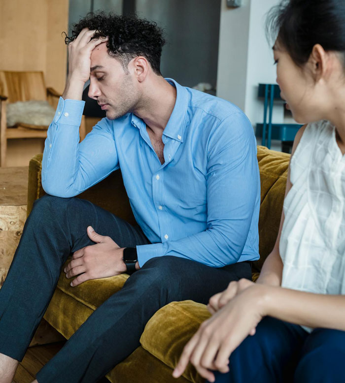 Man in a blue shirt sits with his head in hand, discussing sterilization against partner's wishes.