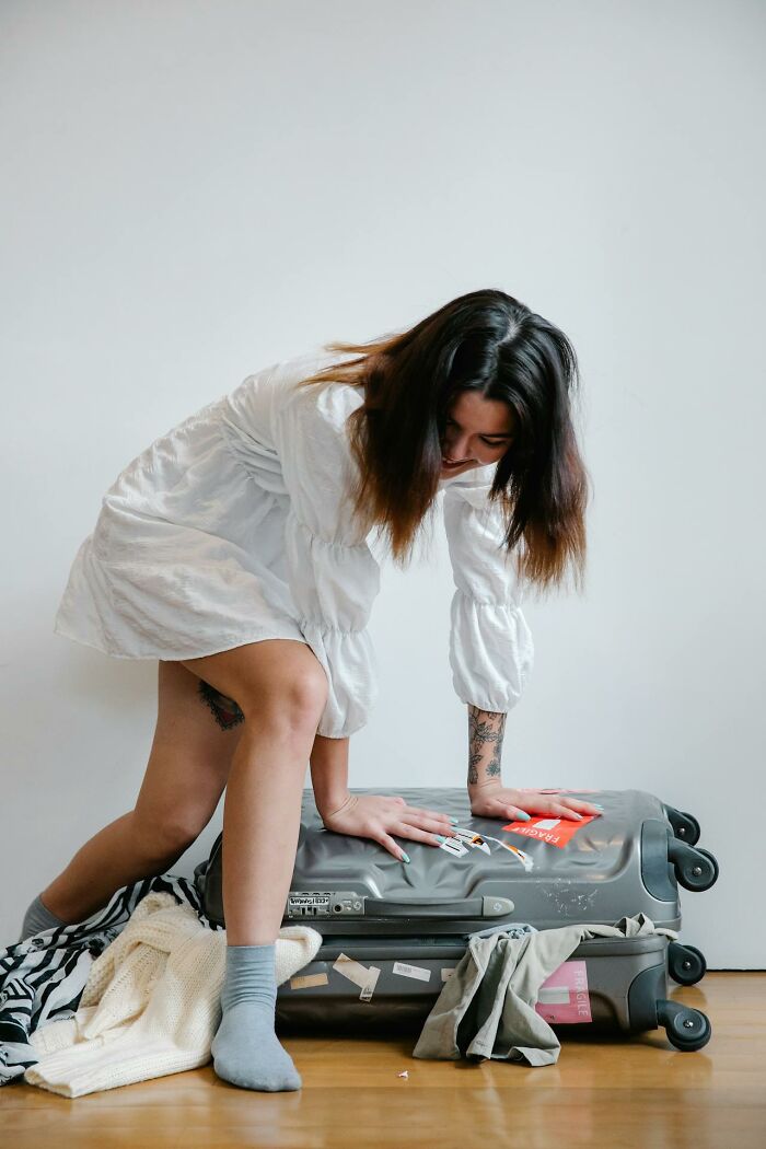 Person kneeling on a packed suitcase, trying to close it.