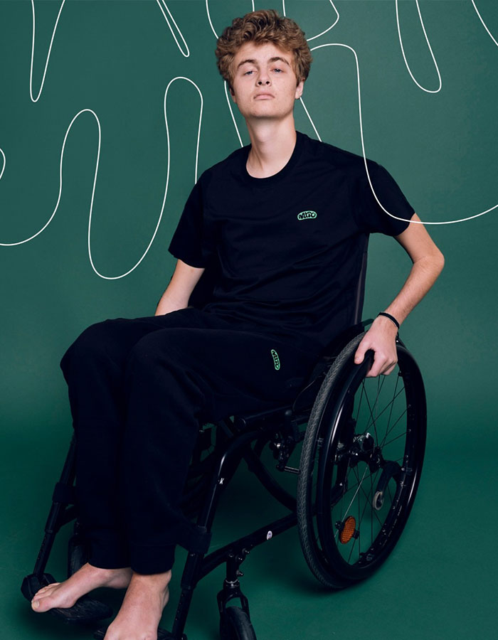 Young man in a wheelchair on a green background, wearing a black outfit, representing Prince Frederik.