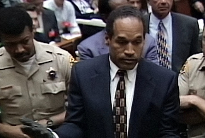 O.J. Simpson in a courtroom scene, escorted by officers, during a significant trial event.