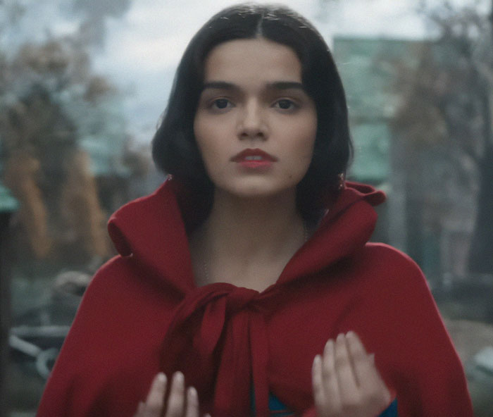 Young woman in a red cloak from Disney's Snow White, gazing forward amid surrounding trees.