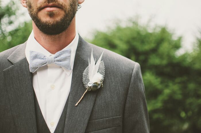 Groom in a grey suit with a bow tie, possibly at a wedding with objections from guests.