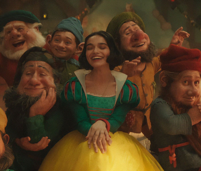 Image of Snow White smiling with seven dwarfs, promoting a Disney movie amid ongoing controversies.