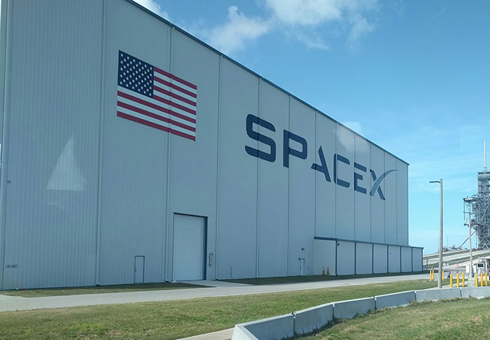 SpaceX facility with American flag, highlighting delayed astronaut rescue mission criticism.