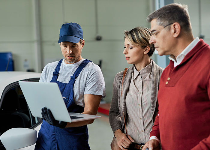 Mechanic shows two professionals a laptop in a workshop, illustrating malicious compliance at work.