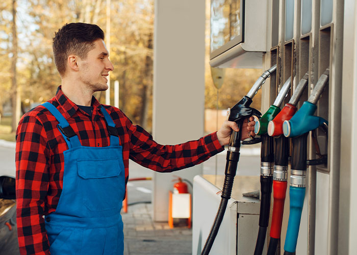 Man in red plaid shirt fueling at a gas station pump.