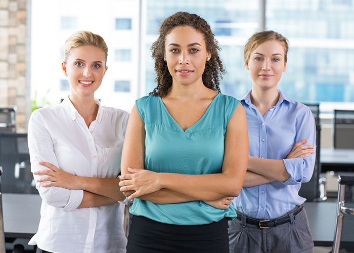 Three professional women standing confidently in an office setting.