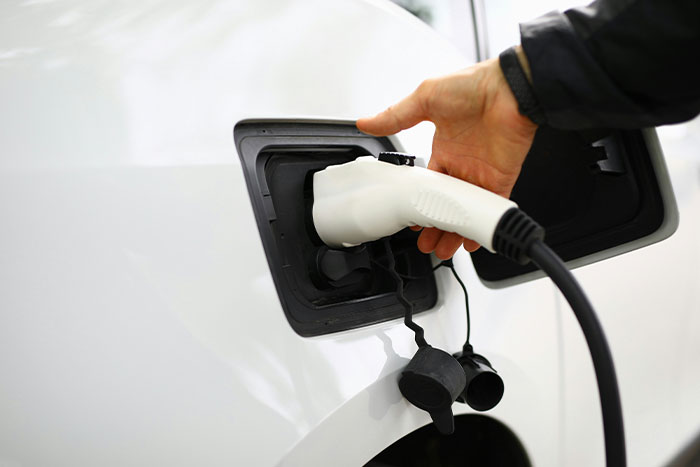 Hand plugging charger into white Tesla at a charging station.