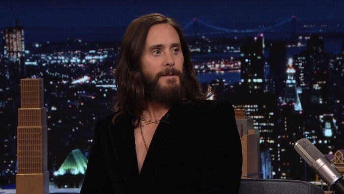 Man with long hair and beard on a talk show set, discussing petty reasons related to celebrities.