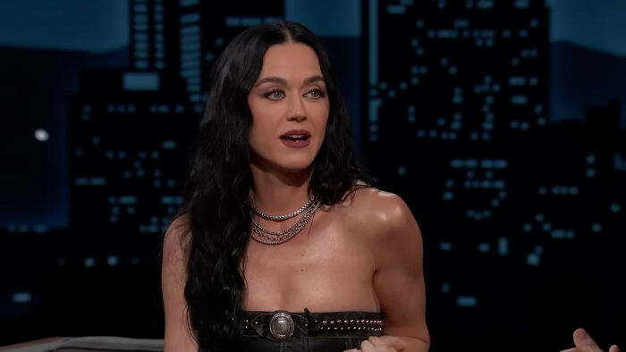 A celebrity with long black hair talks on a late-night show, related to petty reasons for fame.