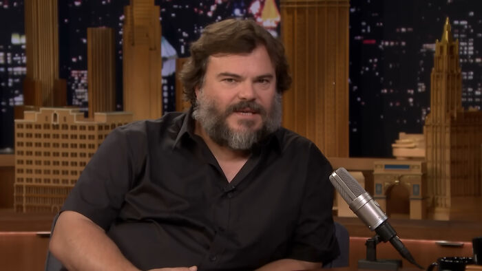 Man in a black shirt with a beard, speaking into a microphone on a talk show set, discussing reasons for celebrity grudges.