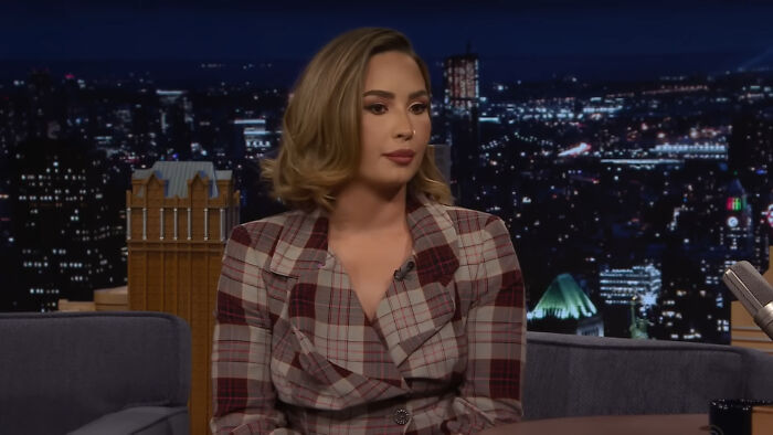 A celebrity in a plaid blazer on a talk show set, discussing a petty incident.